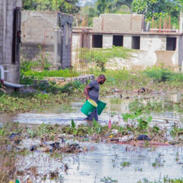 EkoLakay client carrying waste containers through flood waters